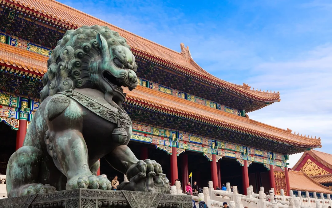 A bronze guardian lion in front of the Forbidden City's main gate in Beijing on a clear day.