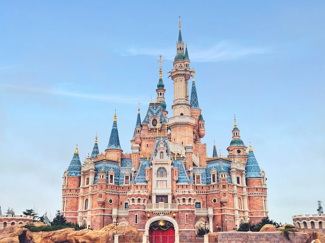 Shanghai Disneyland's castle at dusk with colorful lights and visitors in the plaza.